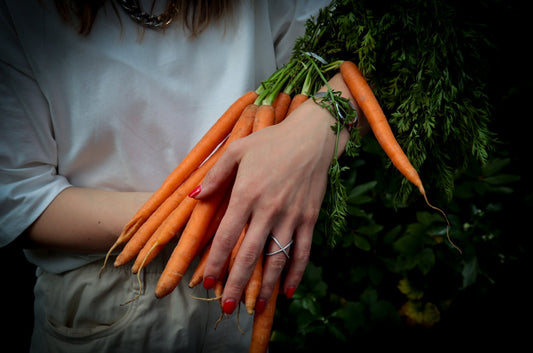 Carrot with greens in hand, red nails, a ring, white T-shirt.