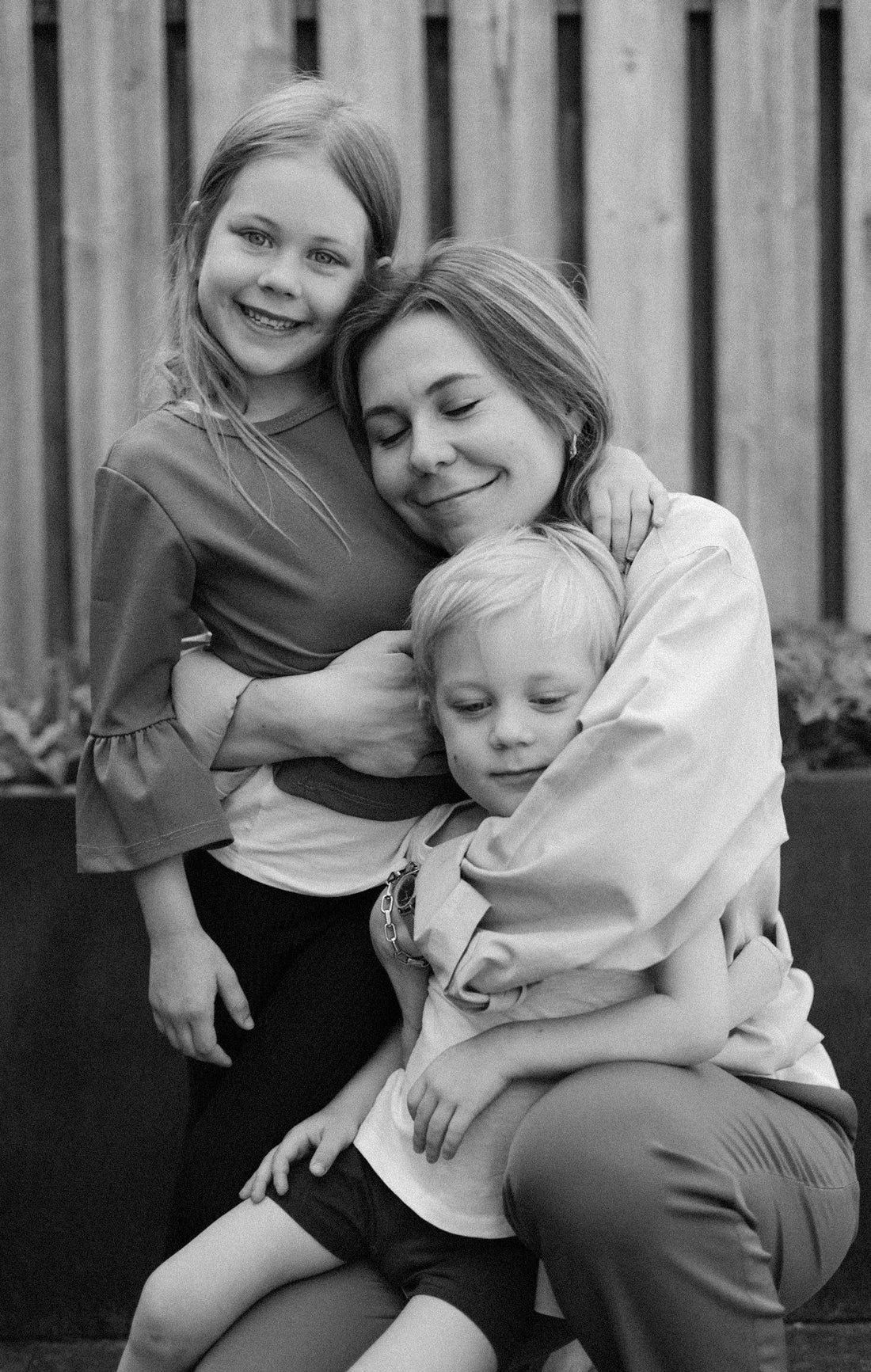 Black-and-white photo: a woman is hugging two children, a boy and a girl.