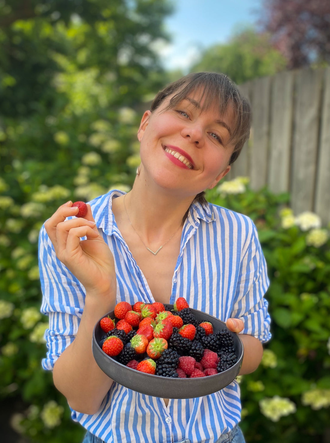 woman in a white-blue shirt with a plate full of berries in the garden