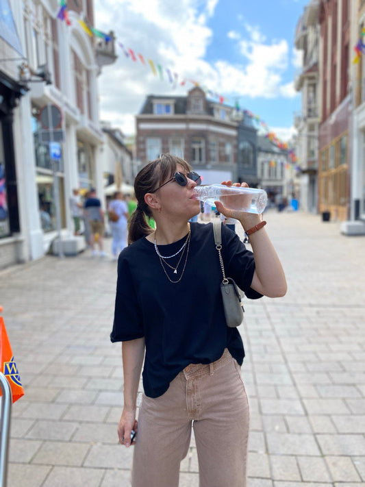 woman on the street is drinking water from a bottle, black t-shirt, beige jeans