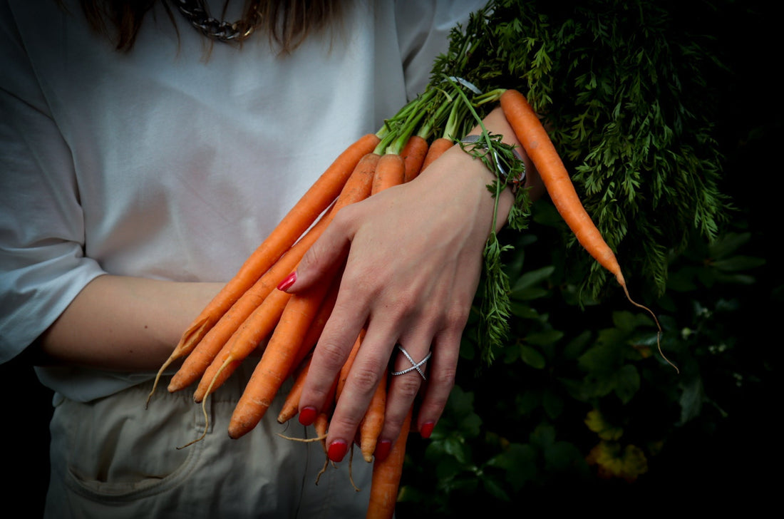 Carrot with greens in hand, red nails, a ring, white T-shirt.
