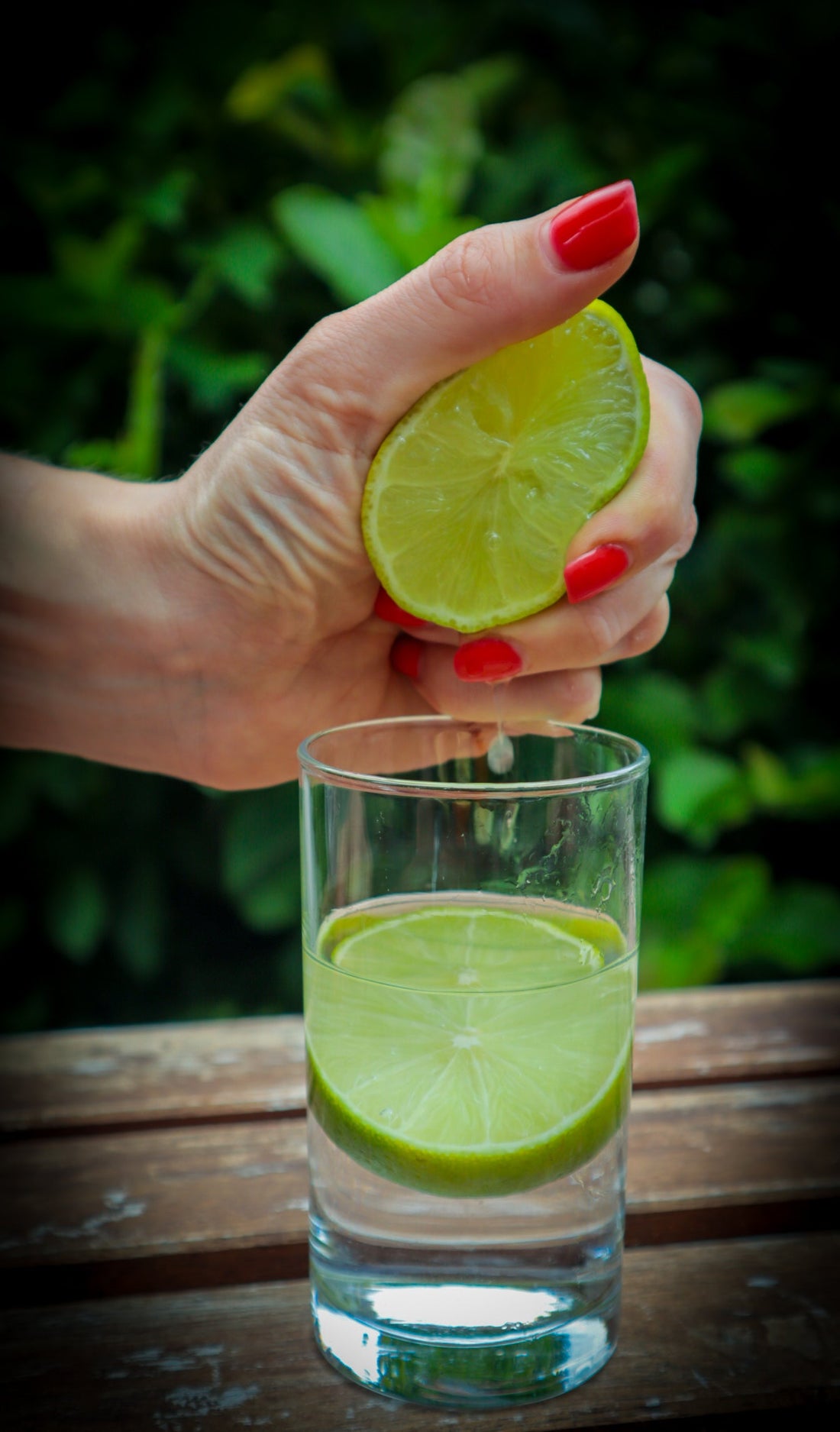 squeezing lime into a glass of water red nails 