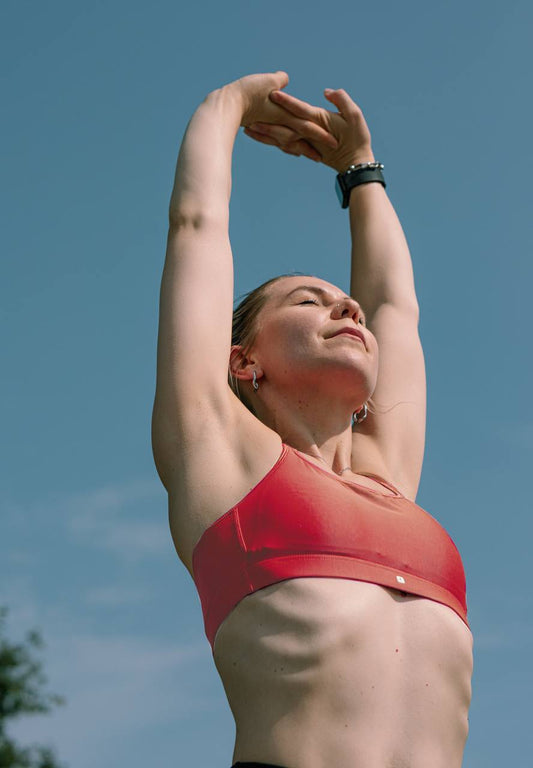 A woman in a pink top is stretching against the backdrop of a blue sky.
