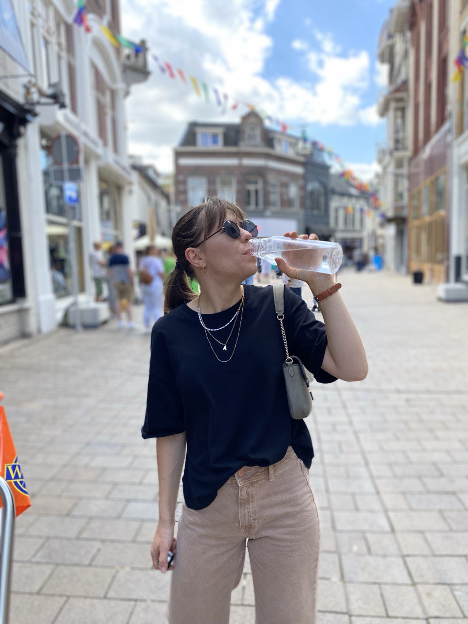 woman on the street is drinking water from a bottle, black t-shirt, beige jeans